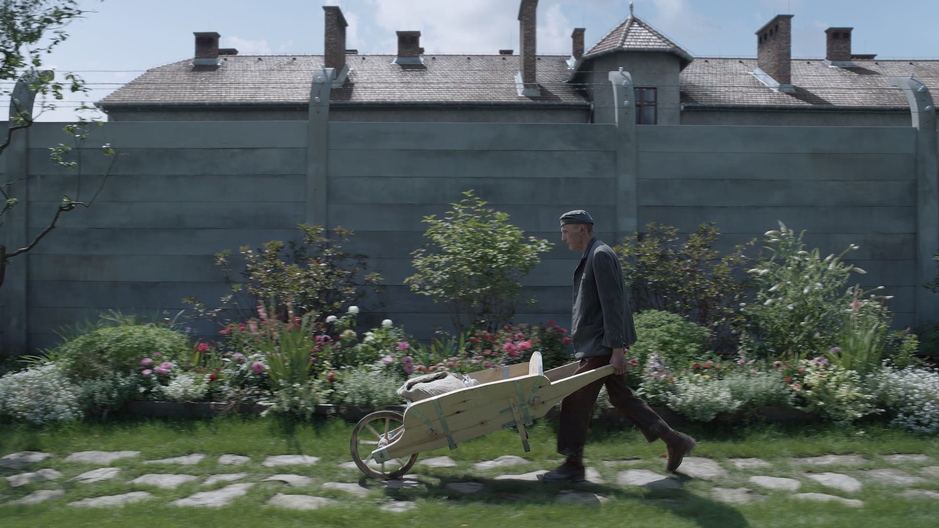 Still from The Zone of Interest: a man pushes a wheelbarrow through a garden